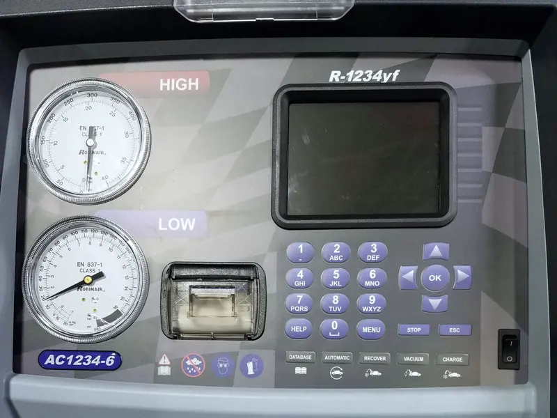 The control panel of an automotive A/C service machine: two analogue gauges marked HIGH and LOW, a dark display, a receipt printer and a purple keypad