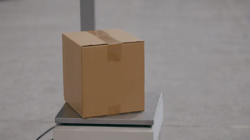 A plain cardboard box sealed with clear tape, sitting on a steel platform scale