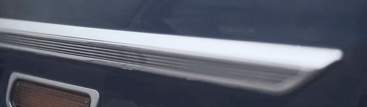 A strip of chrome trim across glossy dark blue paint, a small amber tail light below it