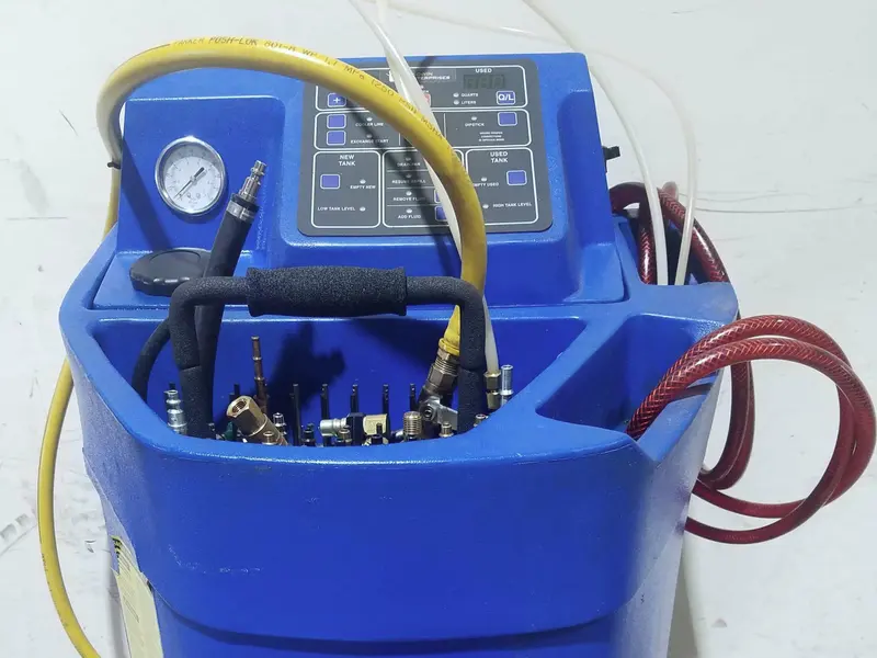 A blue rotomoulded transmission fluid exchange machine with a small control panel and gauge on top, a tray of quick connect adapters, a yellow hose coiled over the top and red hoses on the right